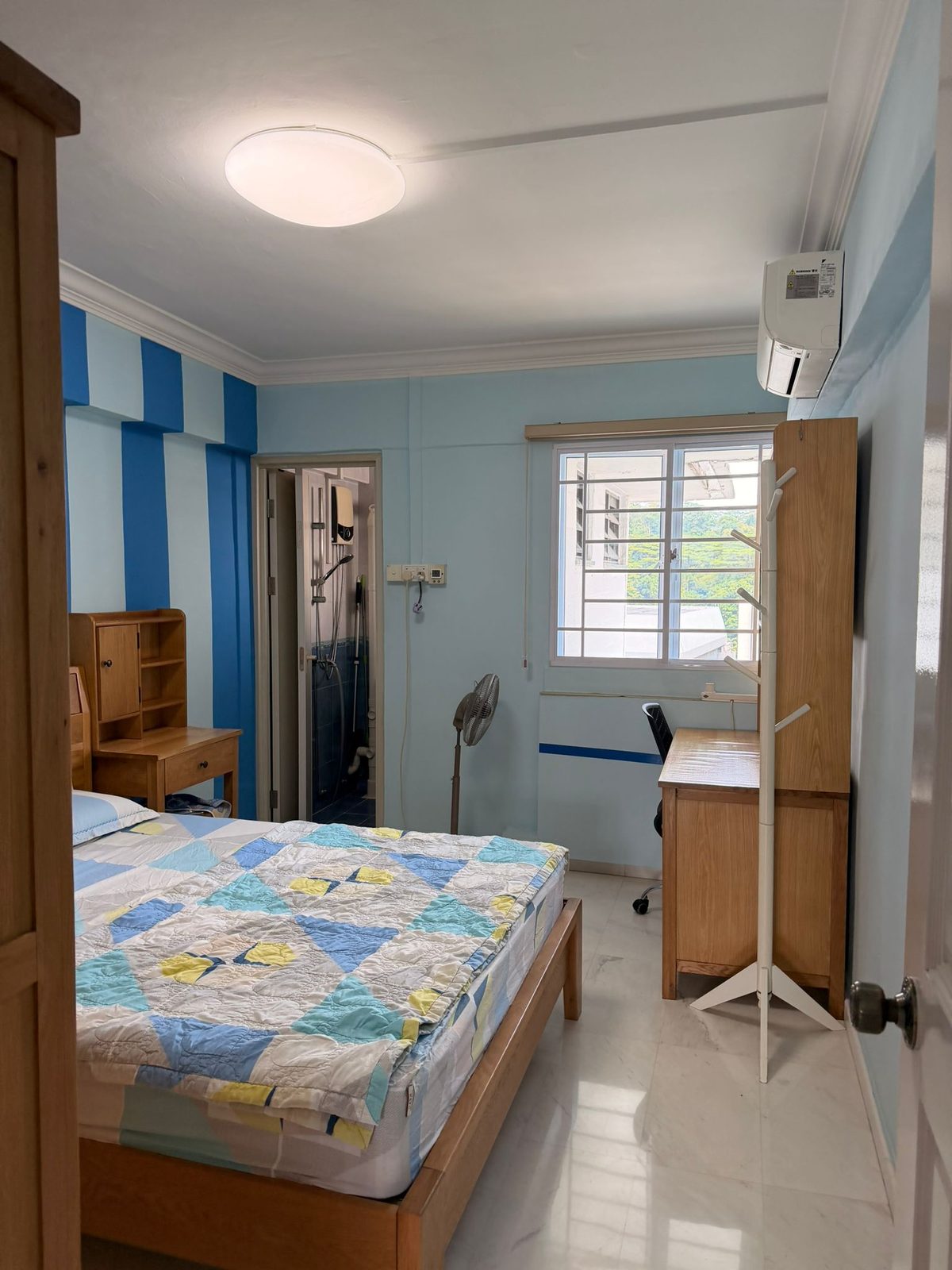 Bright furnished master bedroom with bed, window, air-conditioning, and attached bathroom entrance